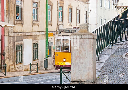 LISBON, PORTUGAL - MAY 2, 2012: The vintage yellow tram of popular E28 route hides behind the column of the handrail in the street of old Alfama neigh Stock Photo