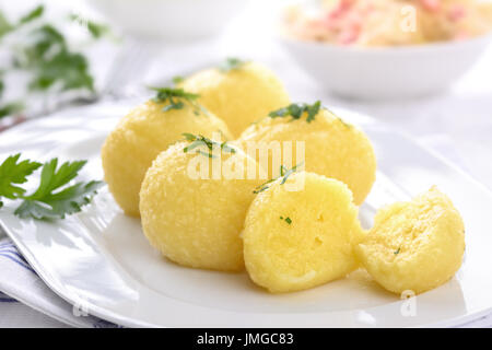 Freshly cooked potato dumplings served on a white platter, sauerkraut with bacon strips in the background Stock Photo