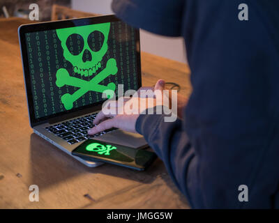 Hacker in hoodie is using a computer. Mobile is also infected. Stock Photo