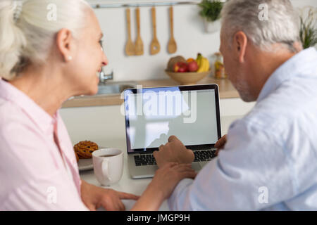 Back view picture of mature loving couple family sitting at the kitchen using laptop computer. Looking aside. Stock Photo
