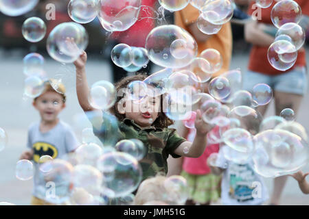A street artist makes soap bubbles whilst children try to burst them in the evening at the main market in Krakow (Poland). Taken 22.06.2017. The second-biggest city in Poland was European City of Culture in 2000. Photo: Jan Woitas/dpa-Zentralbild/dpa | usage worldwide Stock Photo