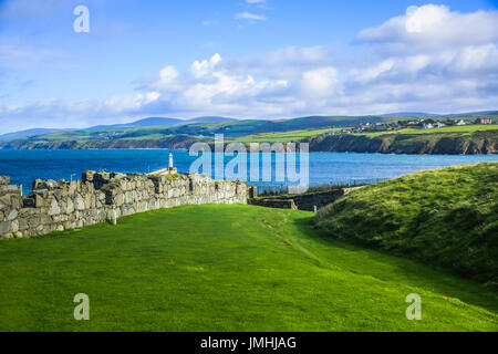 Great wall of Peel Castle constructed by vikings at Peel hill covered with green grass and beautiful coastline of Isle of Man in background Stock Photo