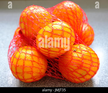 Small oranges in red netting bag Stock Photo