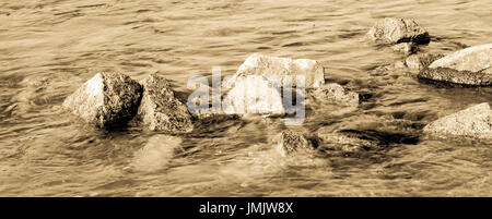 Stones looking out of the water. Image is bright and sepia toned. Stock Photo