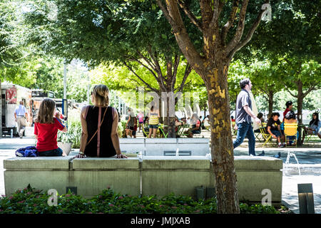 Residents escape the mid day heat under the shade of oak trees at Klyde Warren Deck Park in downtown Dallas Texas Stock Photo