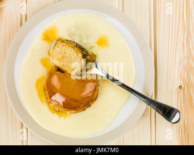 Syrup or Treacle Sponge Pudding With Custard Against A Light Pine Wood Background Stock Photo