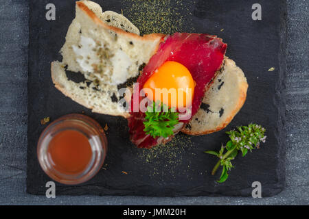 Spanish tapas with slices cured meat and yolk, close view from tiop. Dark photo. Stock Photo