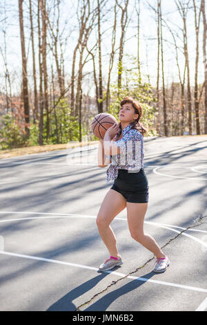 Young fit woman jumping up throwing basketball into hoop in playground Stock Photo