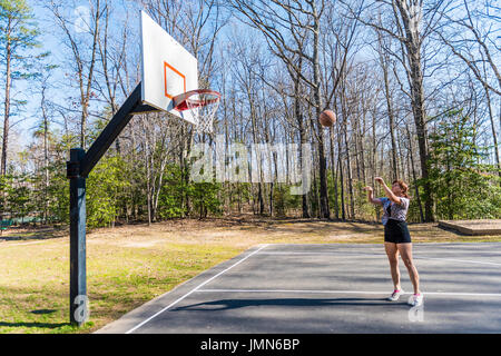 Young fit woman jumping up throwing basketball into hoop in playground Stock Photo