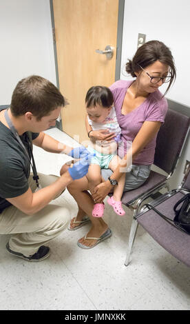 baby being held by anxious mother receiving vaccination injection in doctor's office Stock Photo