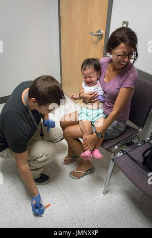 baby being held by anxious mother receiving vaccination injection in doctor's office Stock Photo