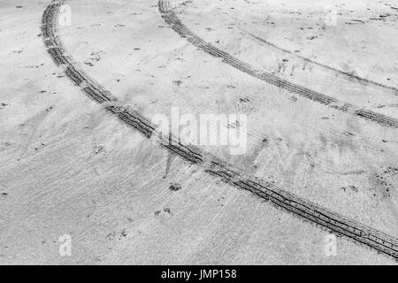 Black and white image of curved/ curving tyre tracks in damp beach sand in Cornwall, UK. Curved tracks, curving tire marks. Stock Photo