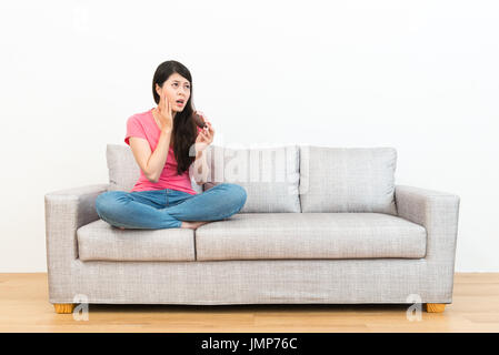 sweet beauty girl looking at white background feeling unhappy when she eating sugar donut sitting on sofa getting tooth painful. Stock Photo