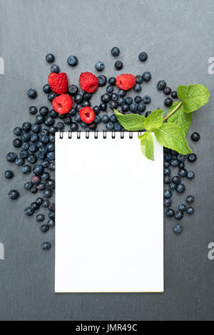 Blueberries, raspberries, mint and notepad for writing notes or resolutions, concept of diet, slimming, detox, healthy lifestyles and nutrition. Mock up, space for text. Stock Photo