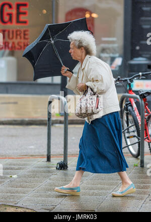 Elderly lady woman in the rain and wind holding an umbrella. Stock Photo