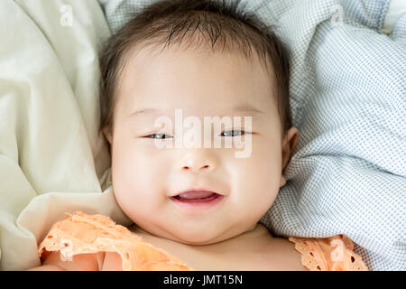 Portrait of a little adorable infant baby girl lying on back on blanket and looking in camera indoors Stock Photo