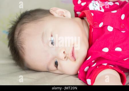 Portrait of a little adorable infant baby girl lying on back on the bed indoors Stock Photo