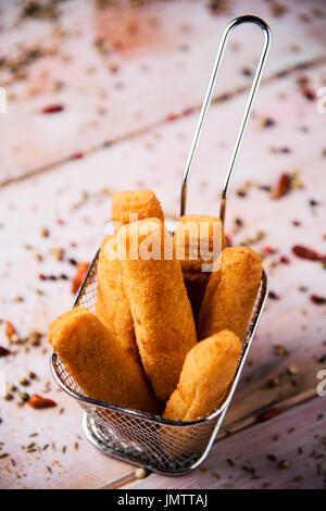 some appetizing fish sticks served in a metal basket, on a rustic wooden table Stock Photo