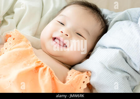 Portrait of a little adorable infant baby girl lying on back on blanket and looking in camera indoors Stock Photo