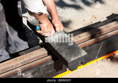 Man working on light rail construction site, cutting vibration damping material for tram rail tracks noise reduction Stock Photo