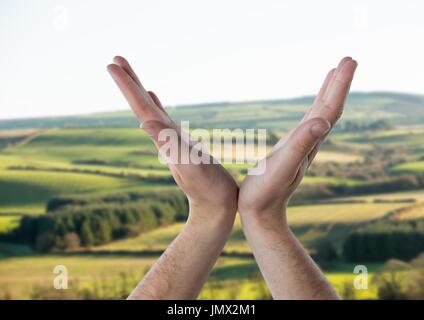 Digital composite of Hands opened in V shape over green landscape Stock Photo