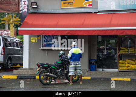 A man standing by his motorcycle in front of a store. Medellin, Colombia, South America. Stock Photo