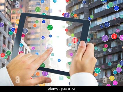 Digital composite of Holding tablet and City with icons colorful floating in sunset Stock Photo