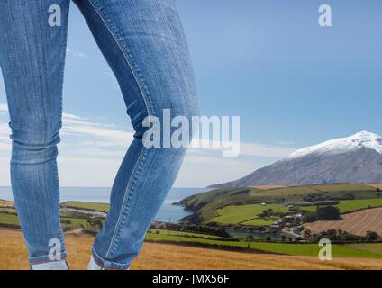 Digital composite of Woman's legs in jeans in front of nature landscape Stock Photo