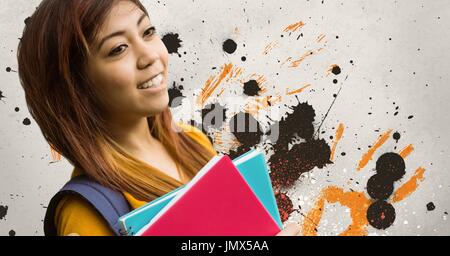 Digital composite of Happy young student woman holding notebooks against grey, yellow and black splattered background Stock Photo