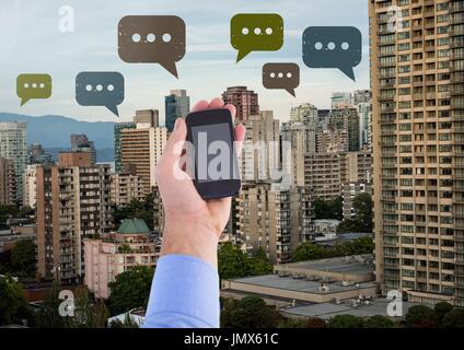 Digital composite of Holding phone and Chat bubble icons over city Stock Photo