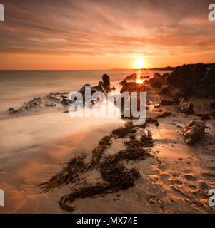 A dramatic beach, rock and seaweed sunset taken close to the summer solstice on the beautiful island of Anglesey. Stock Photo