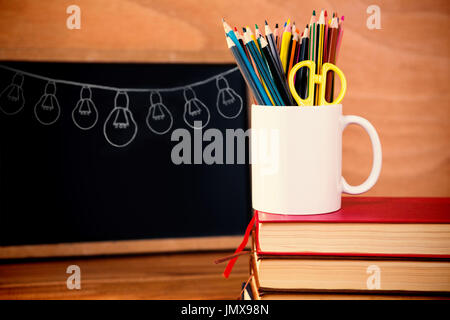 Illustration image of light bulbs arranged against desk organizer on stack of books against blackboard Stock Photo