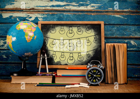 Light bulbs on black splash against empty blackboard with school supplies Stock Photo