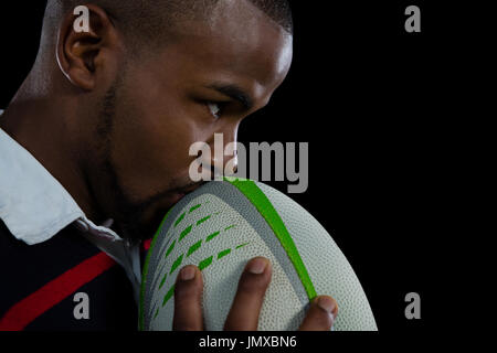 Close up of male player kissing rugby ball against black background Stock Photo