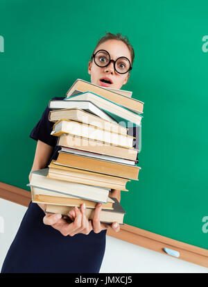Astonished student with pile of books in her hands, staring at you with her mouth open. Photo of young girl wearing glasses. Back to school! Stock Photo