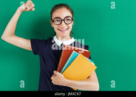 Smiling student hugging books and showing her biceps. Photo of teen near blackboard, education concept Stock Photo