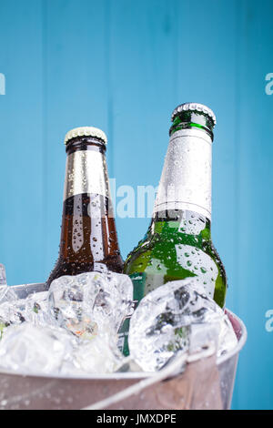 Three unopened bottles of beer inside metal bucket filled with iced Stock Photo