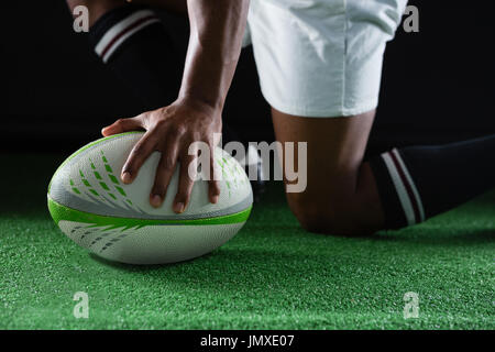 Side view of sportsman kneeling while holding rugby ball on field Stock Photo