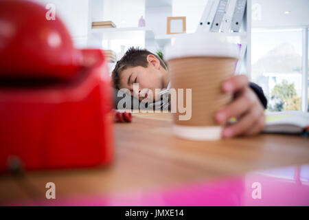 Boy as business executive sleeping while holding coffee cup in office Stock Photo