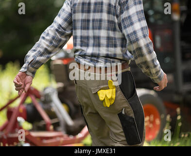 Close up of gardener pocket with sticking protective glover, Tractor with mower in background in public park Stock Photo