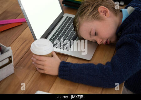 Boy as business executive sleeping while holding coffee cup in office Stock Photo