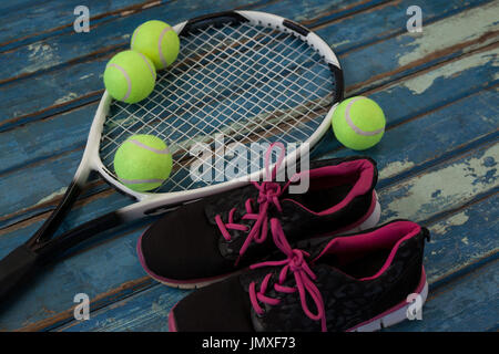 High angle view of black sports shoes by tennis balls and racket on blue wooden table