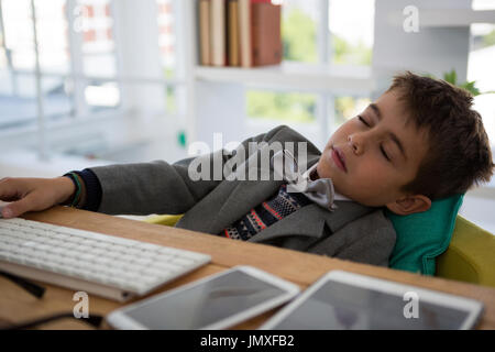 Boy as business executive sleeping in office Stock Photo