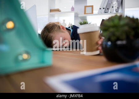 Boy as business executive sleeping while holding coffee cup in office Stock Photo