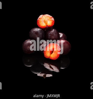 Stack of purple plums isolated on a black glossy background with real reflection Stock Photo