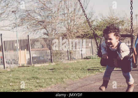 Little girl is having fun on the swing in her local playground. Stock Photo