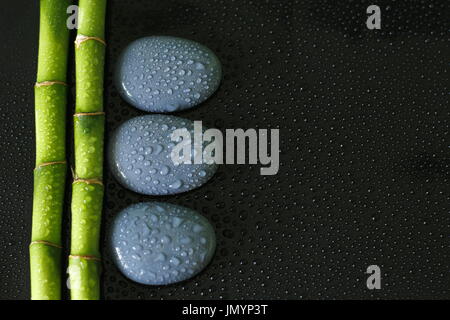 Black background with bamboo branch on the left and gray zen pebbles with drops of water Stock Photo