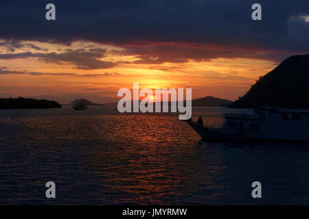 Silhouette of people sitting on ships watching the ocean sunset waiting for the giant bats to come out at night in Flores, Indonesia