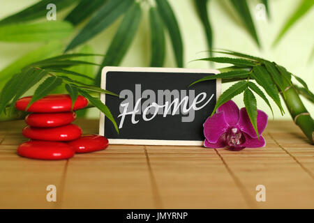 Red pebbles arranged in Zen lifestyle with an orchid, a lighted candle, a bamboo branch and foliage with the message home on the slate Stock Photo