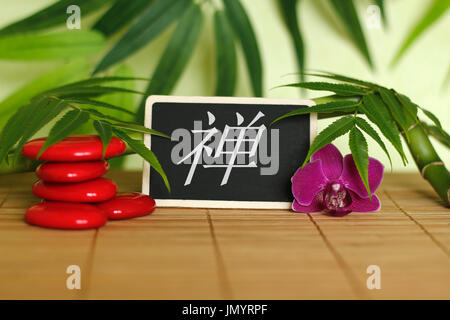 Red pebbles arranged in Zen lifestyle with an orchid, a lighted candle, a bamboo branch and foliage with the message zen on the slate Stock Photo